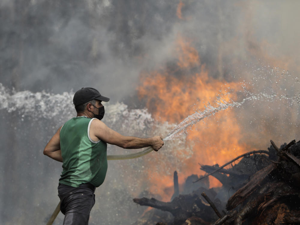 A local resident uses a garden hose to try to stop a forest fire from reaching houses in the village of Figueiras, outside Leiria, central Portugal, Tuesday, July 12, 2022.