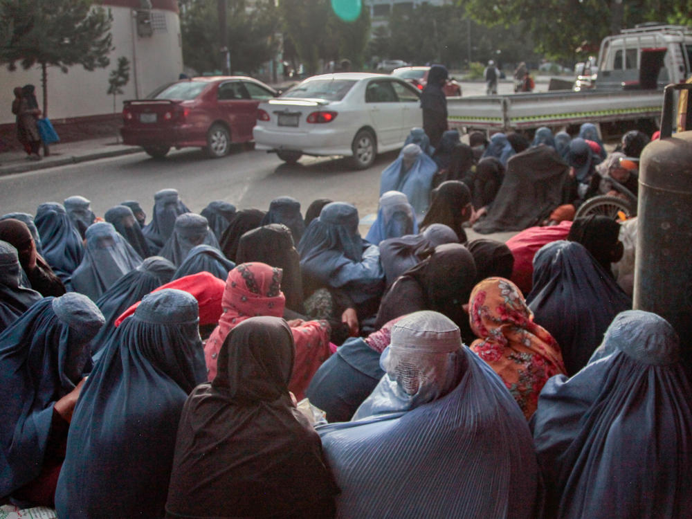 Women in burkas sit outside a bakery in Kabul. Impoverished women from hilltop slums around Kabul have been flocking to bakeries in the city, silently waiting to see if someone will purchase bread for them.