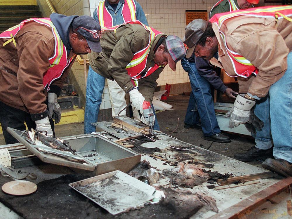 Transit workers dismantle the charred inner wall of a token booth at the Kingston Avenue and Fulton Street subway station in the Bedford-Stuyvesant section of Brooklyn, on Nov. 26, 1995, after attackers sprayed a flammable liquid into the token booth and lit it on fire, according to police.