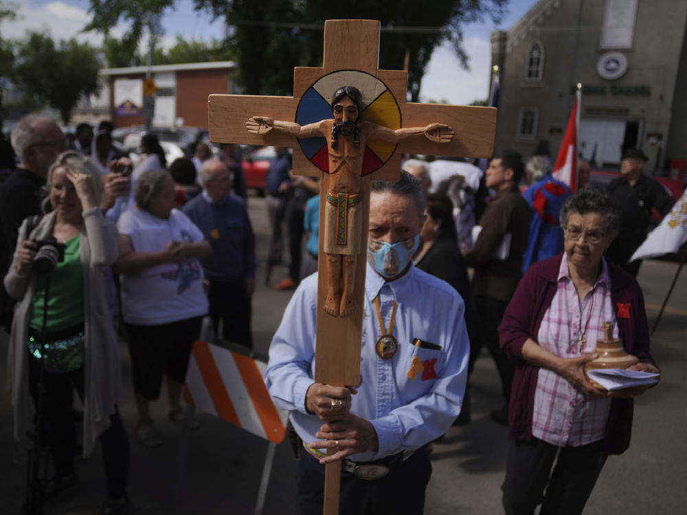 Elmer Waniandy raises the crucifix as he leads his fellow parishioner into the rededicated and newly renovated Sacred Heart Church of the First Peoples sanctuary, July 17, 2022, in Edmonton, Alberta.