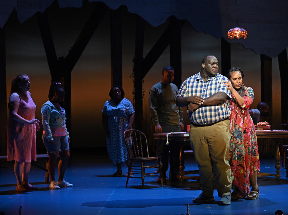 Patience (Talise Trevigne, right) comforts Castor (Reginald Smith Jr.) after his breakdown over the crush of dept and his search for a solution as other family members look on.