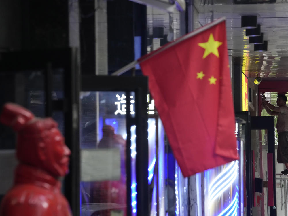 A worker stands on a platform near a Chinese national flag, Friday, July 15, 2022, in Beijing. China's economy contracted in the three months ending in June compared with the previous quarter after Shanghai and other cities shut down to fight coronavirus outbreaks, but the government said a 