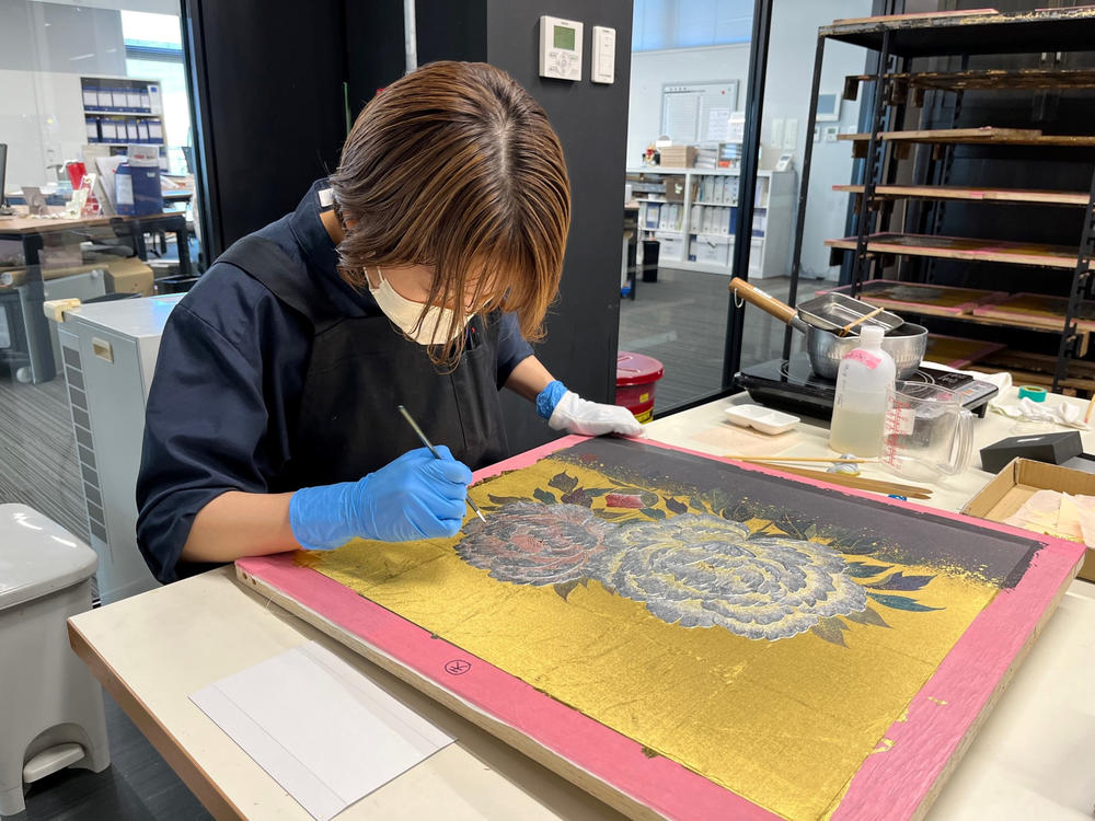 An employee at the Hakuichi factory applies gold leaf to a painting.