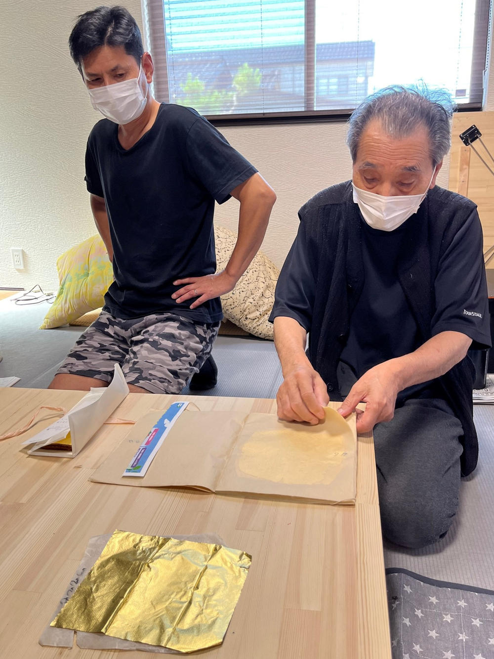 Yoshikazu Netsuno (right) displays a flattened piece of gold leaf at his small factory in Kanazawa while his son Shinichi looks on.