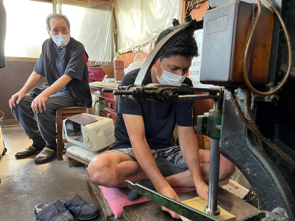 Yoshikazu Netsuno (left) watches his son Shinichi hammer a thick stack of specialized paper. In between each sheet is a thin layer of gold leaf. 