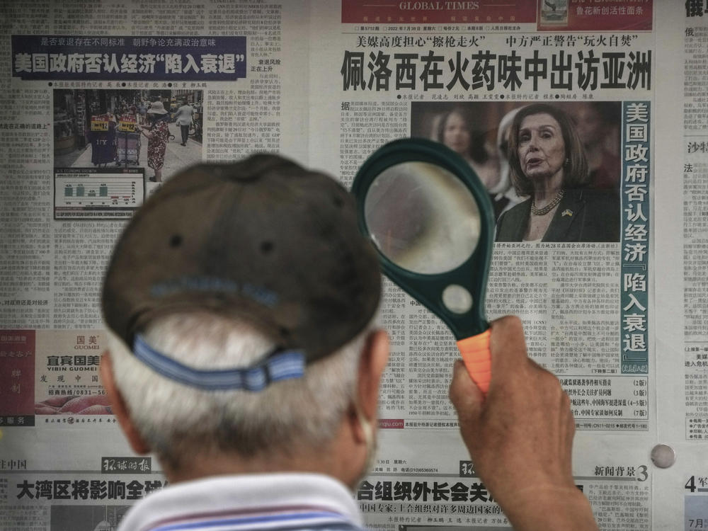 A man uses a magnifying glass to read a newspaper headline reporting on U.S. House Speaker Nancy Pelosi's Asia visit, at a stand in Beijing, Sunday, July 31, 2022.