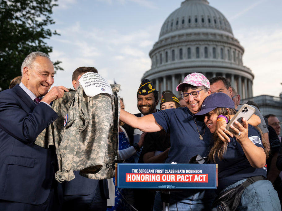 Senate Majority Leader Chuck Schumer (D-N.Y.) looks on Tuesday as Susan Zeier, mother-in-law of the late Sgt. First Class Heath Robinson, hugs Rosie Torres, wife of veteran Le Roy Torres, who suffers from illnesses related to his exposure to burn pits in Iraq, after the Senate passed the PACT Act at the U.S. Capitol in Washington.