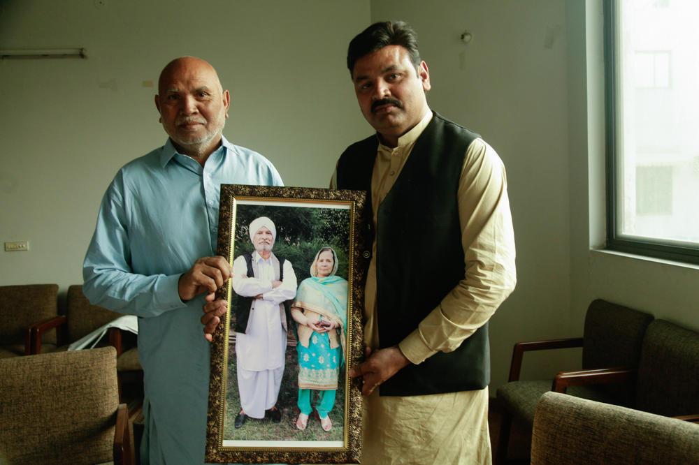 Shahid Masih and his father, Rafik, hold up a picture of Rafik's uncle and his wife, whose descendants they met in February at a border crossing after decades of separation. The reunion was arranged by Papinder Singh. Rafik's father, Iqbal, who hoped to meet the children and grandchildren of his Indian siblings, passed away before the reunion occurred.