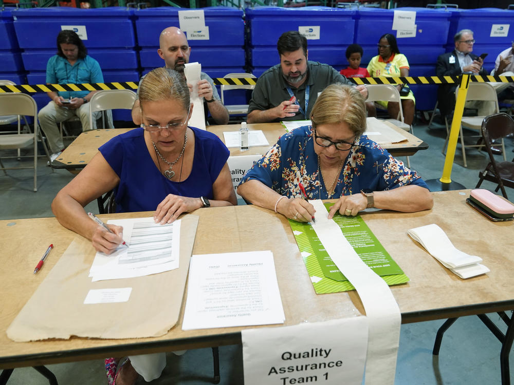 Miami-Dade County Elections Department employees check the tabulation made by voting equipment that will be used in the upcoming state primary election.