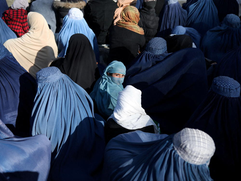 A girl sits in front of a bakery in the crowd with Afghan women waiting to receive bread in Kabul on Jan. 31, 2022.