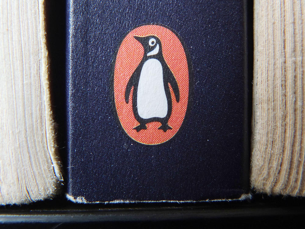 The Penguin logo is visible on the spine of a book. The U.S. Department of Justice is suing Penguin Random House and Simon & Schuster to block the companies from completing a merger valued at $2.175 billion.