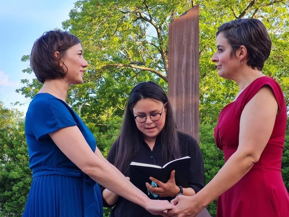Carlie Brown (left) and Molly Pela exchange wedding vows as their friend, Julie Takahashi, officiates the ceremony. Both women said they rushed to get married after reading Supreme Court Justice Clarence Thomas' concurring opinion in striking down <em>Roe v. Wade</em>, in which he suggested also overturning the landmark case that legalized same-sex marriage.