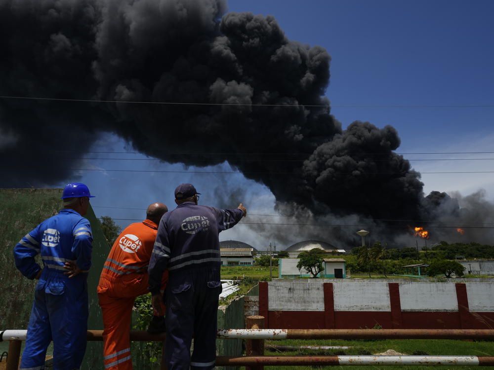 Workers of the Cuba Oil Union, known by the Spanish acronym CUPET, watch a huge rising plume of smoke from the Matanzas Supertanker Base, as firefighters work to quell a blaze which began during a thunderstorm the night before, in Matazanas, Cuba, Saturday, Aug. 6, 2022.