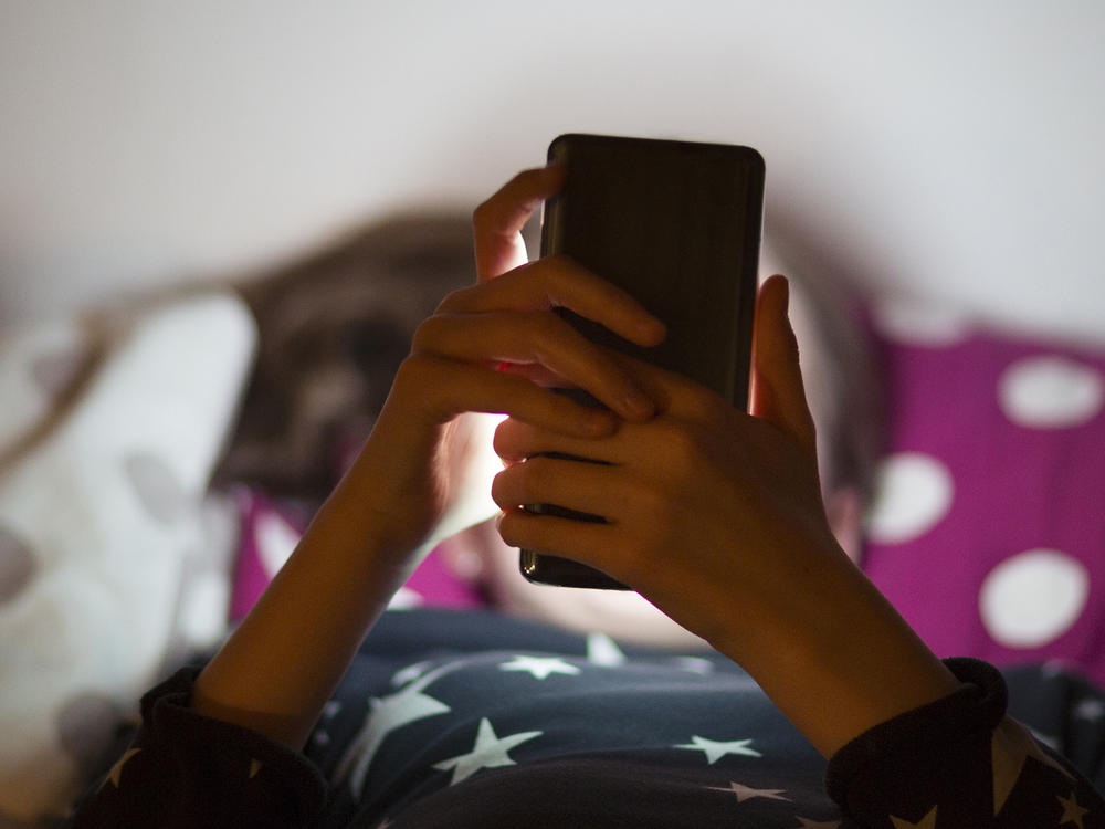 Snapchat is rolling out new parental controls that allow parents to see their teenager's contacts and confidentially report to the social media company any accounts that concern them. A child lies in bed illuminated by the glow of a cell phone.