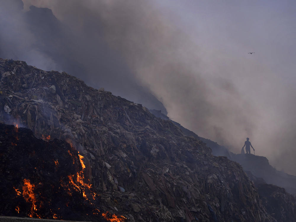 A person picks through trash for reusable items as a fire rages at the Bhalswa landfill in New Delhi, April 27, 2022.