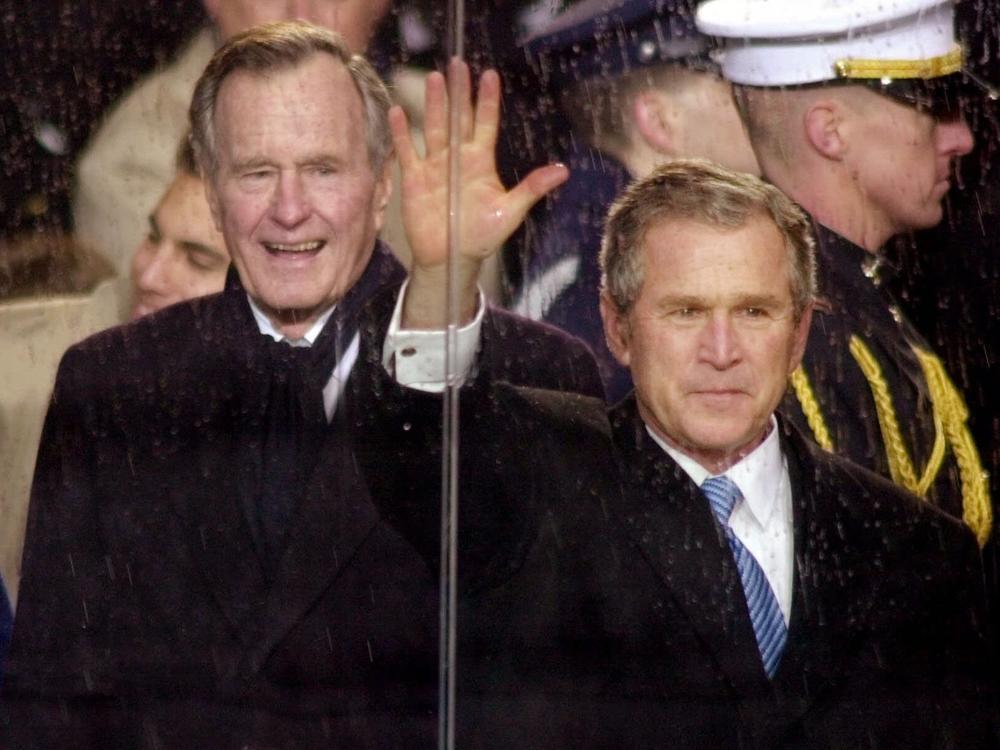 In this Jan. 20, 2001, file photo, standing in the rain, President George W. Bush waves as he watches his inaugural parade pass by the White House viewing stand in Washington, Saturday afternoon, Jan. 20, 2001. With him are his wife and first lady Laura Bush and his father, former President George H.W. Bush.