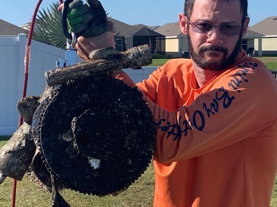 Jose Torres holds up a boat propeller, boat trailer roller, and a flywheel from a motor found in Tampa Bay.