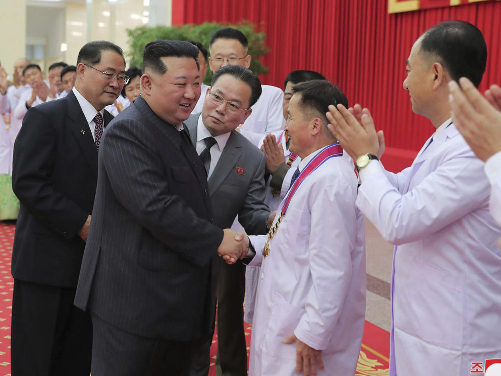 In this photo provided by the North Korean government, North Korean leader Kim Jong Un shakes hands with a health official in Pyongyang, North Korea, Wednesday, Aug. 10, 2022.