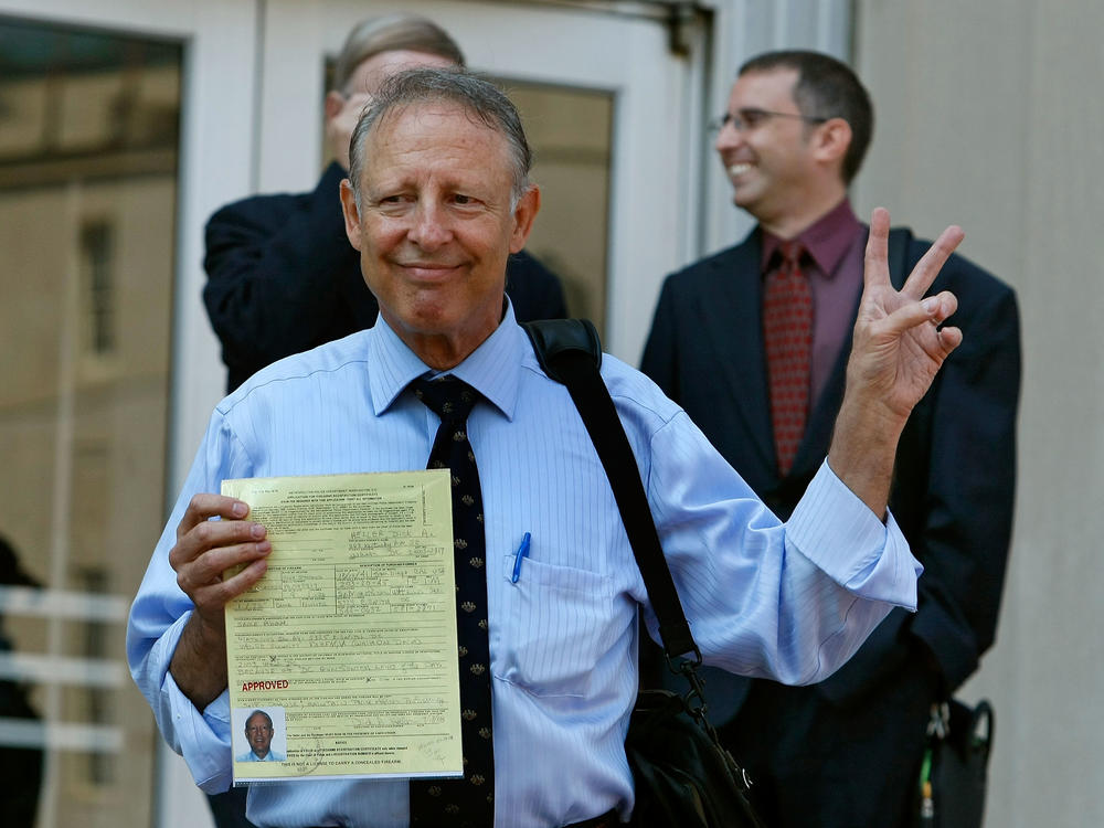 Dick Heller, plaintiff in the Supreme Court case <em>District of Columbia v. Heller</em>, gestures while holding his newly approved gun permit at the District of Columbia Police Department in August 2008, weeks after the Supreme Court ruled in his favor.