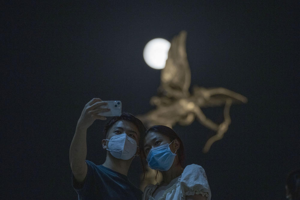 Beijing, China: Residents wearing masks take a selfie near a statue of Cupid as a supermoon rises in the night sky.