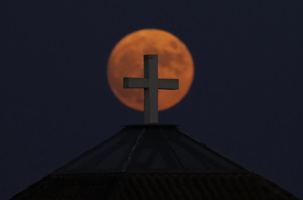 Anthoupolis, Cyprus: The supermoon rises behind a cross on the dome of a Maronite church.