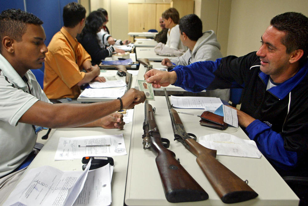 A Brazilian citizen shows his identification card to a Federal Police agent (left) as he trades in two collection rifles as part of a national firearm buyback program, in São Paulo, Brazil, July 23, 2004.