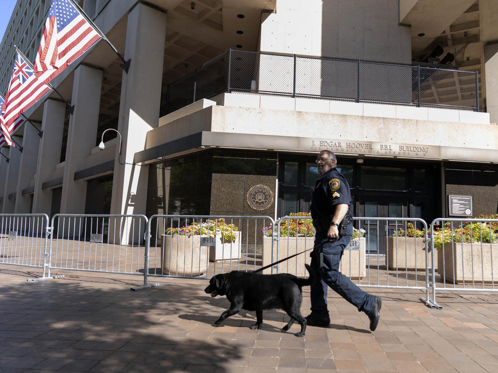A Federal Bureau of Investigation police officer walks with his working dog outside Federal Bureau of Investigation building headquarters in Washington, Saturday, Aug. 13, 2022.