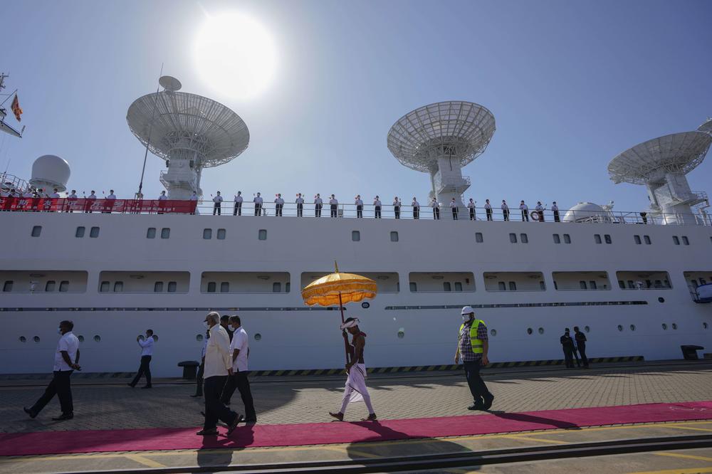 A Sri Lankan traditional dancer carries a decorative umbrella as the crew of Chinese ship Yuan Wang 5 wave Chinese flags after arriving at Hambantota International Port in Hambantota, Sri Lanka, on Tuesday.