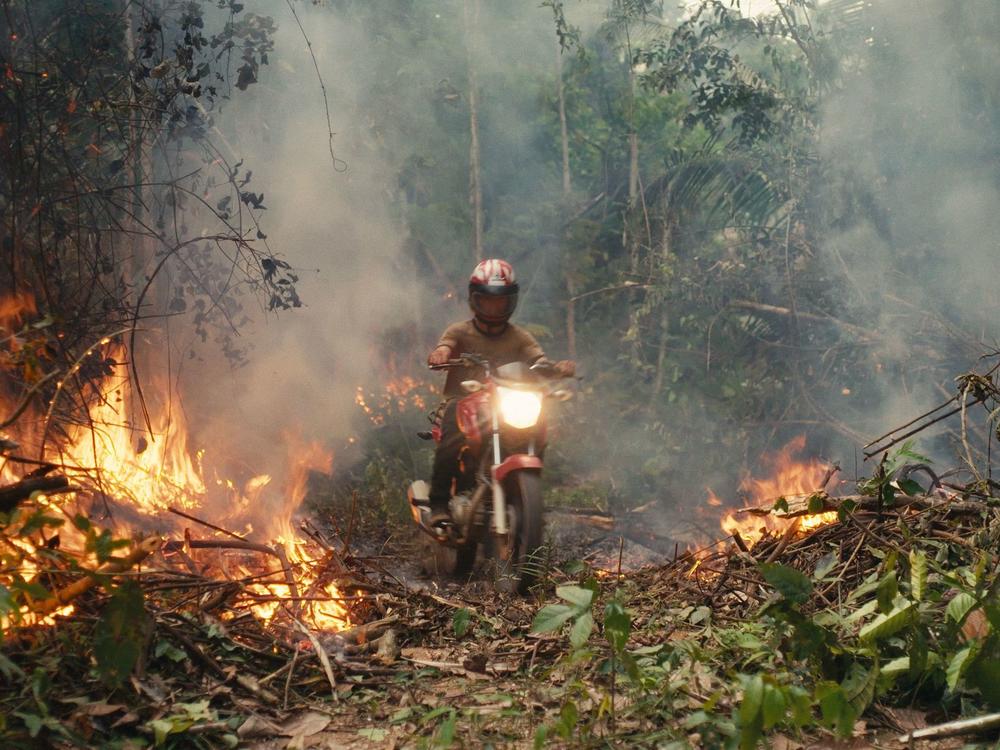 An invader rides his motorcycle through a rainforest blaze.
