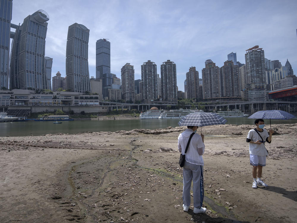 Students carrying umbrellas stand on the dry riverbed of the Jialing River in southwestern China's Chongqing Municipality, Friday, Aug. 19, 2022.