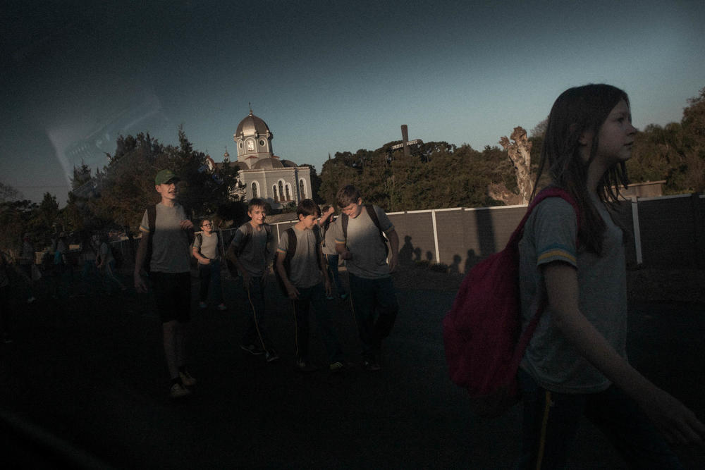 Students leaving school in Prudentópolis. In the background are the Nossa Senhora do Patrocínio Church and the cemetery. The church, built in the mid-1920s, showcases the Byzantine architecture typical of churches in Ukraine.