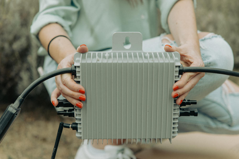 Karolina Attspodina displays the microinverter attached to We Do Solar panels. The microinverter is plugged into a power socket, and the energy from the panels then becomes the initial source of energy for the household, ahead of power from the grid.
