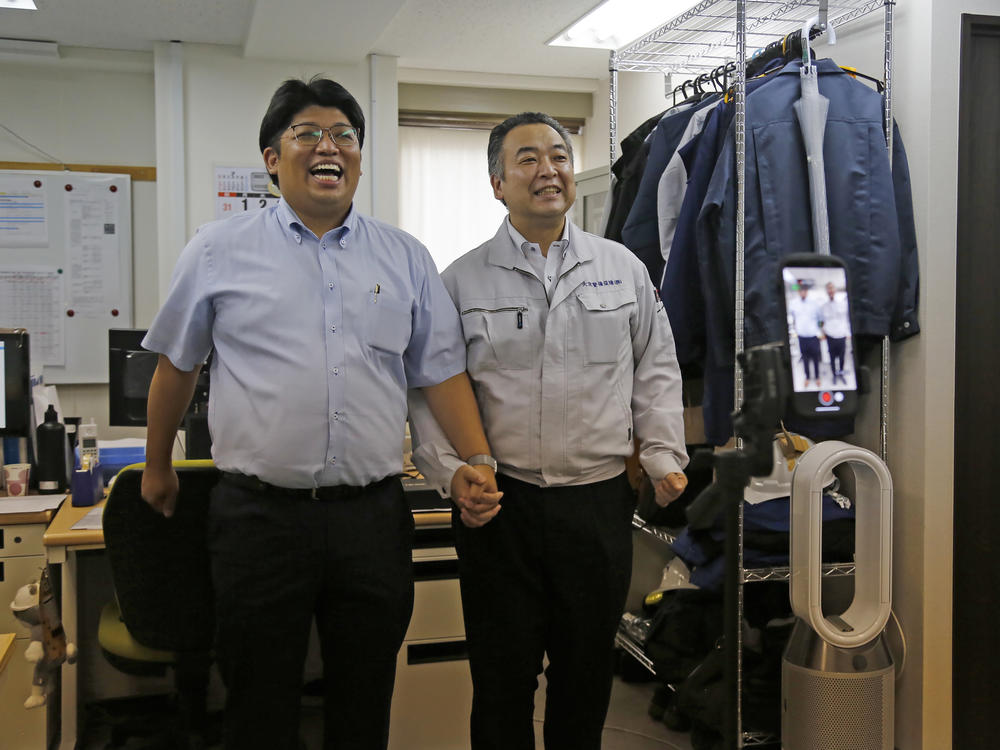 Daikyo Security Chief Executive Daisuke Sakurai, left, and General Manager Tomohiko Kojima take a Tik Tok video together as seen on the screen in the device (right) at the Tokyo headquarters office of Daikyo Security Co. in Tokyo Monday, Aug. 22, 2022.