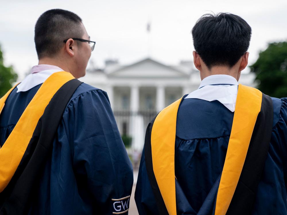 Students from George Washington University wear their graduation gowns outside of the White House in Washington, D.C, on May 18. Economists worry President Biden's plan to forgive student loans could encourage more people to take on debt in the hopes of also being forgiven.