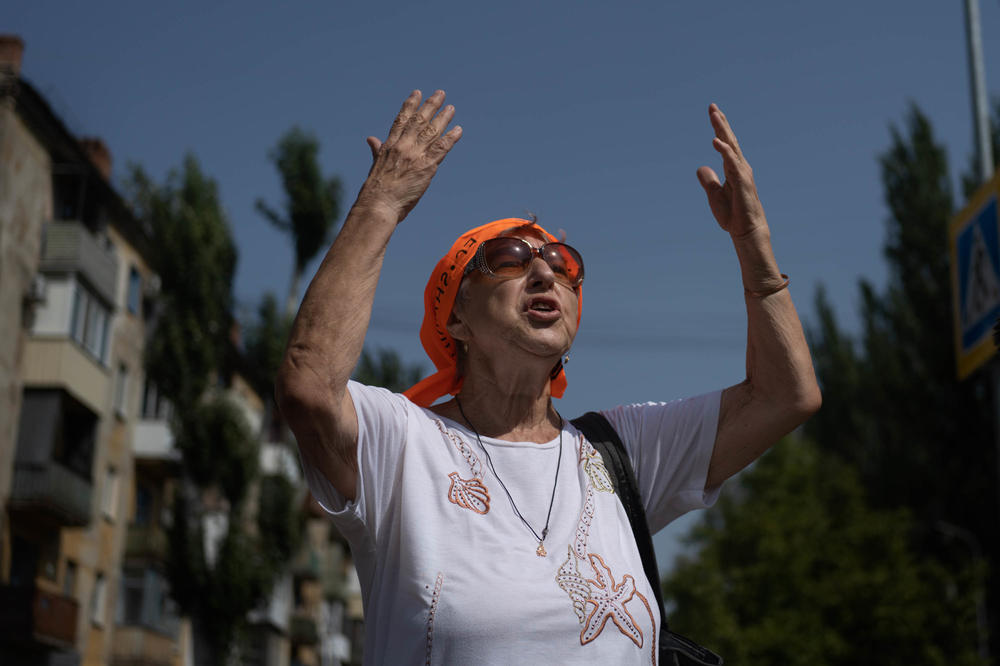 Liubov Mahlii recites a poem she wrote about peace in the Donbas while she stands across from a building that was shelled that morning.