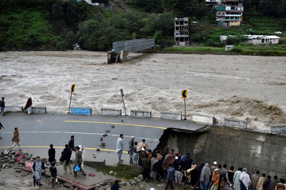 People gather next to a section of a road damaged by flood waters in the Madyan area of Pakistan's northern Swat Valley, on Aug. 27. Thousands of people living near flood-swollen rivers in Pakistan's north were ordered to evacuate.