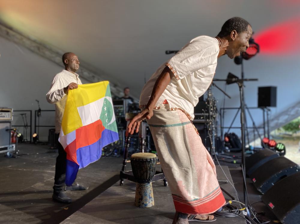 Global musicians can run into daunting red tape when it comes to obtaining a visa to perform at festivals. Soubi Attoumane (left) and M'madi Djibaba (right) of the band Comorian from Comoros had to fly to another country to apply for a U.K. visa to come to Peter Gabriel's WOMAD festival. Above: They unfurl the Comorian flag to a standing ovation at the concert on July 31.