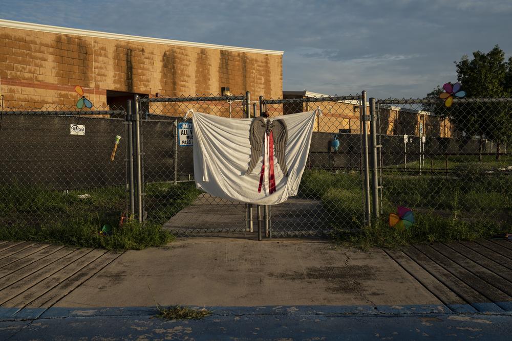 Alas de ángel, rehiletes, y un mantel blanco están expuestos en la entrada donde el tirador entró a Robb Elementary School en mayo.