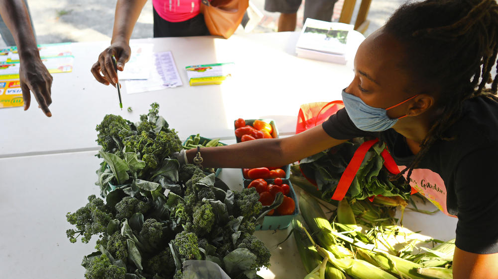 Sabrina Pilet-Jones with the Urban Farming Institute reaches for a carton of broccoli for a customer at a Boston farm stand on Aug. 14, 2020.