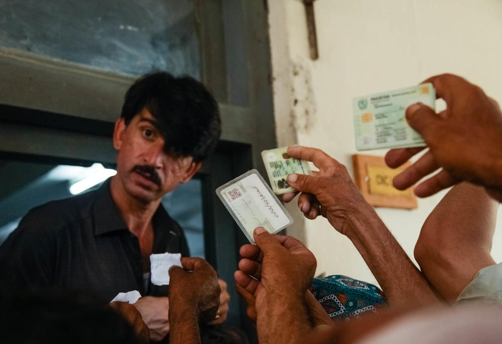A crowd of Pakistanis made destitute or homeless by this summer's flooding produce identification cards to register for temporary shelter and food on the grounds of a technical college.