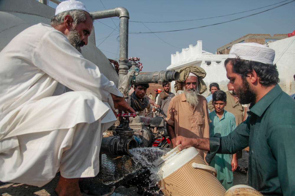 Men line up to fill bottles and wash utensils with water from a government tanker at a flooded area on the outskirts of Nowshera.