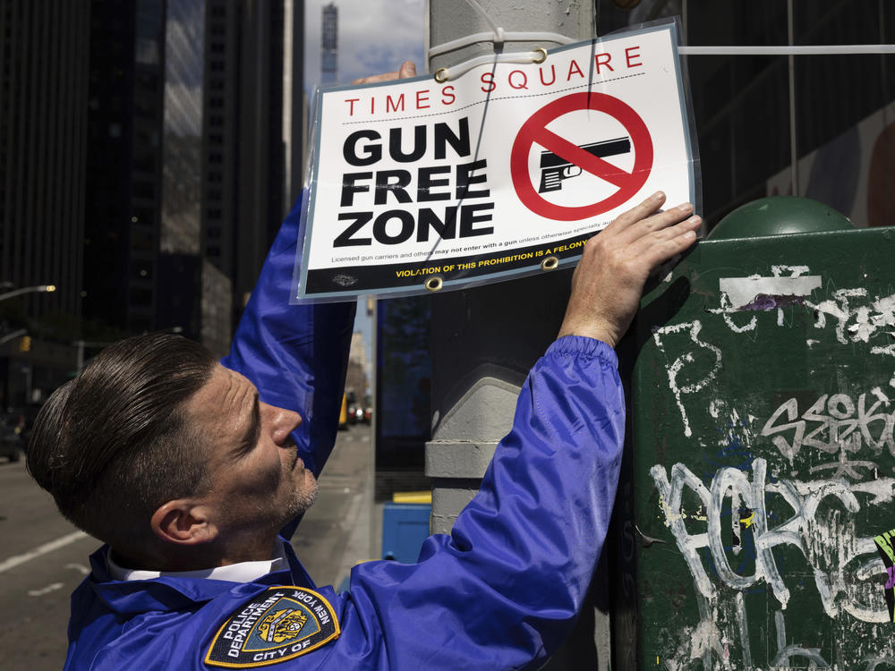 An New York Police Department Public Affairs officer sets up signs reading Gun Free Zone around Times Square, Wednesday, Aug. 31, 2022, in New York.