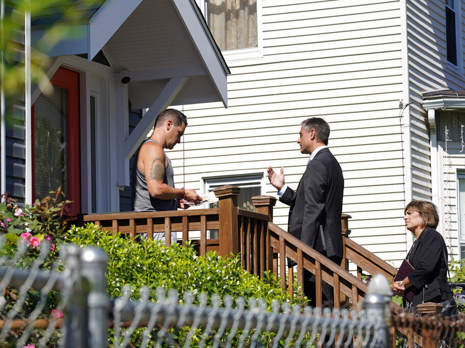 Dan Sideris, center, talks with a resident on a front porch Thursday accompanied by his wife, Carrie Sideris, as the couple returns to door-to-door visits as Jehovah's Witnesses in Boston. Dan Sideris said he had been apprehensive about evangelizing in person in 