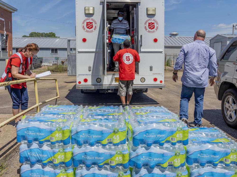 Michelle Hartfield, a public information officer for the Salvation Army, takes notes while Booker Ellis, Chris Bonham and Walter Houston unload water donated by the Salvation Army to the Mississippi Industries for the Blind on Thursday.