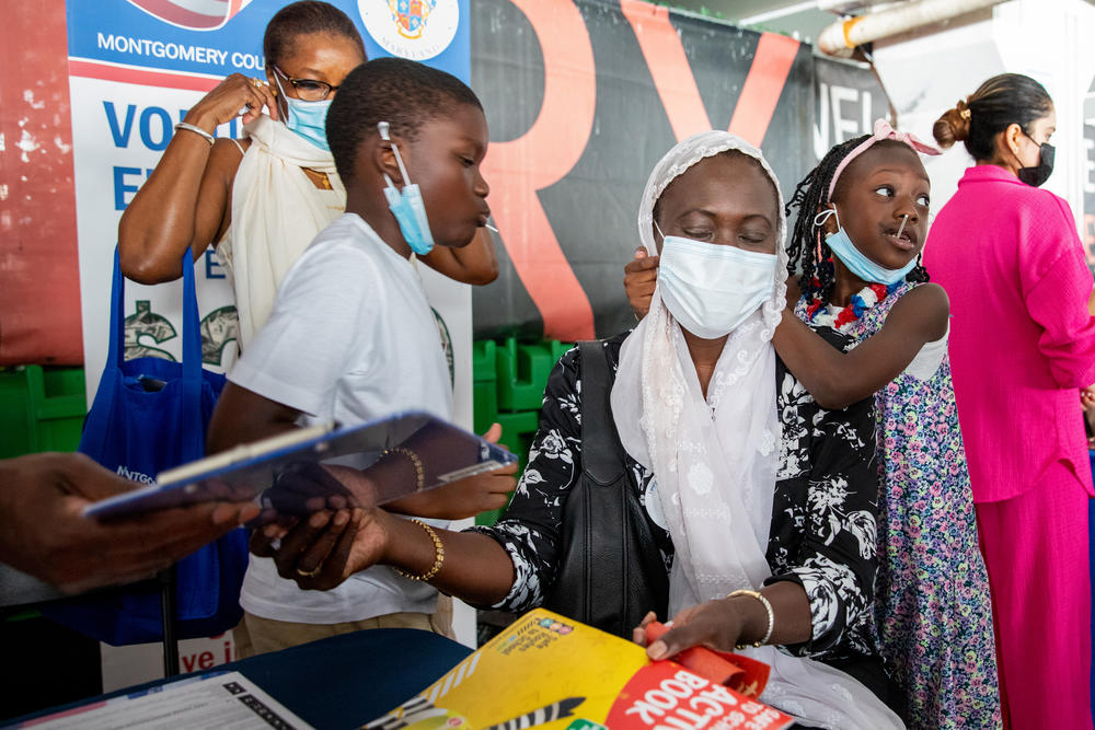 Codou Wade-Drakeford turns in her poll worker application as her 7-year-old daughter, Touty S. Drakeford, grabs onto her with her nephew Mouhamadou Tall and sister Oulimata Toure watching. 