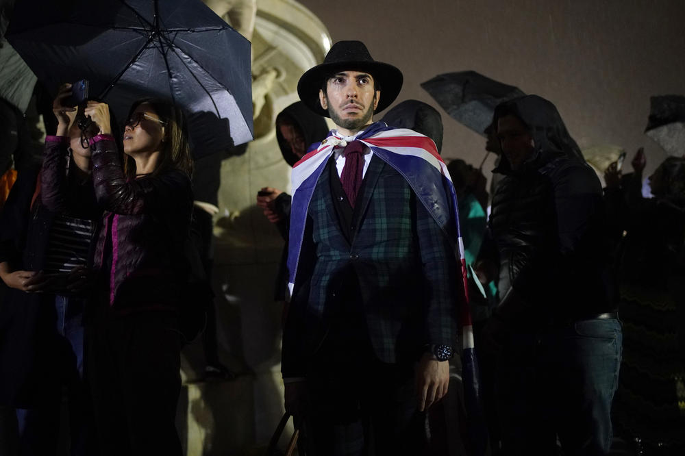 A mourner draped in The Union flag on Queen Victoria Memorial outside Buckingham Palace following the announcement of the death of Queen Elizabeth II on Thursday.