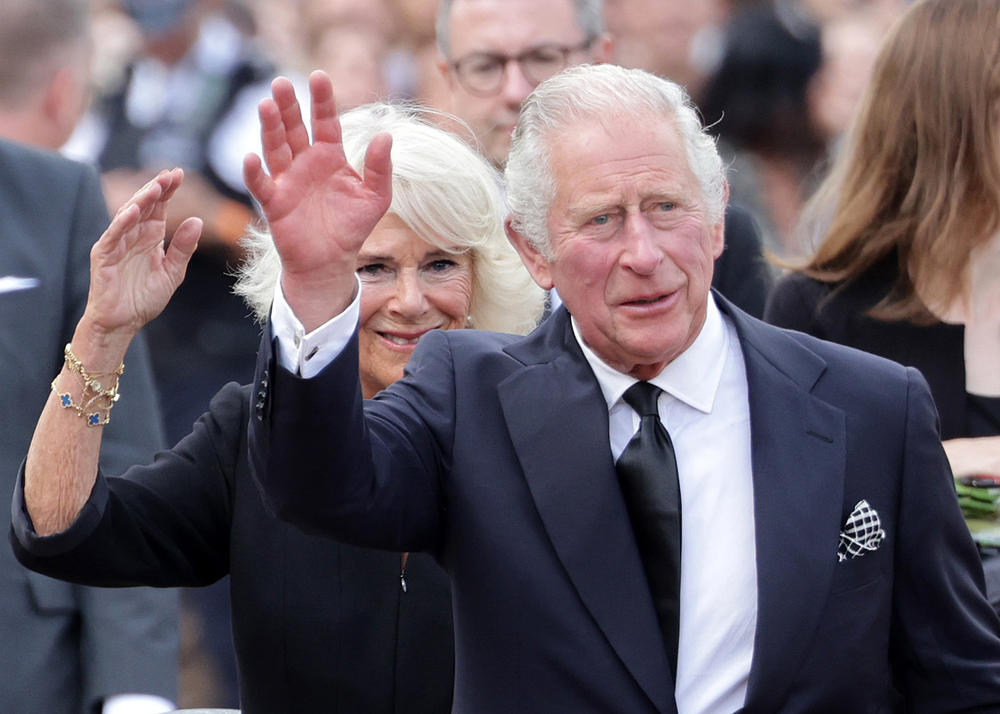 King Charles III and Camilla, Queen Consort, wave after viewing floral tributes to the late Queen Elizabeth II outside Buckingham Palace on Saturday.
