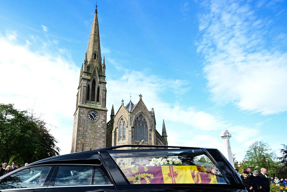 Members of the public pay their respects as they hearse carrying the coffin of Queen Elizabeth II, draped in the Royal Standard of Scotland, is driven through Ballater.