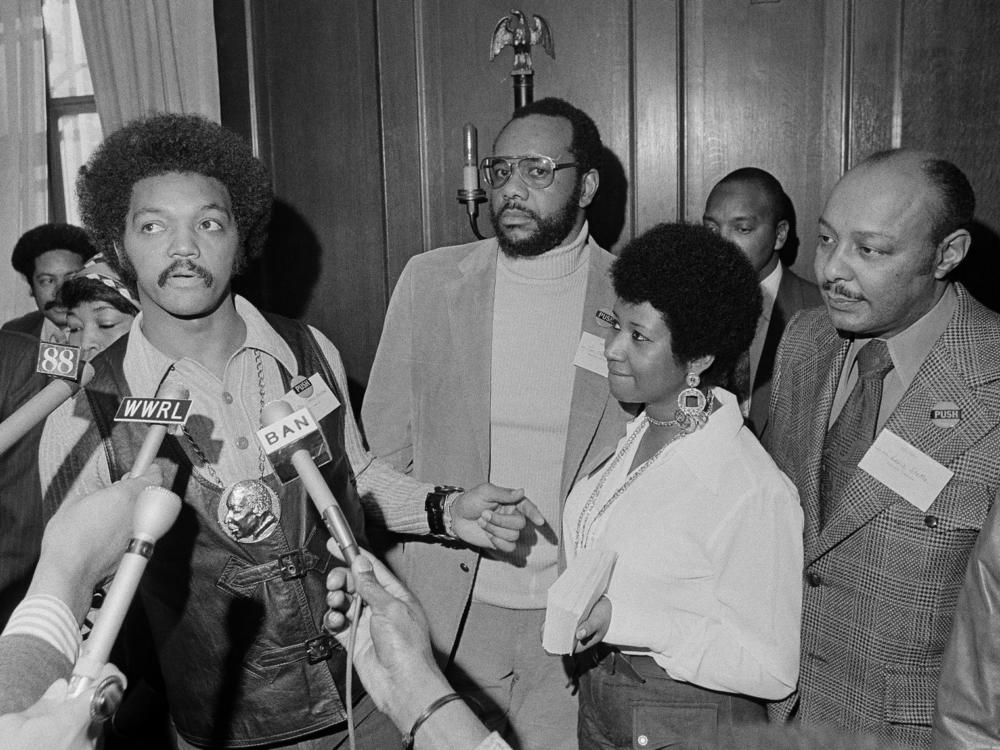 This March 26, 1972 file photo shows the Rev. Jesse Jackson speaking to reporters at the Operation PUSH Soul Picnic in New York as Tom Todd, vice president of PUSH, from second left, Aretha Franklin and Louis Stokes.
