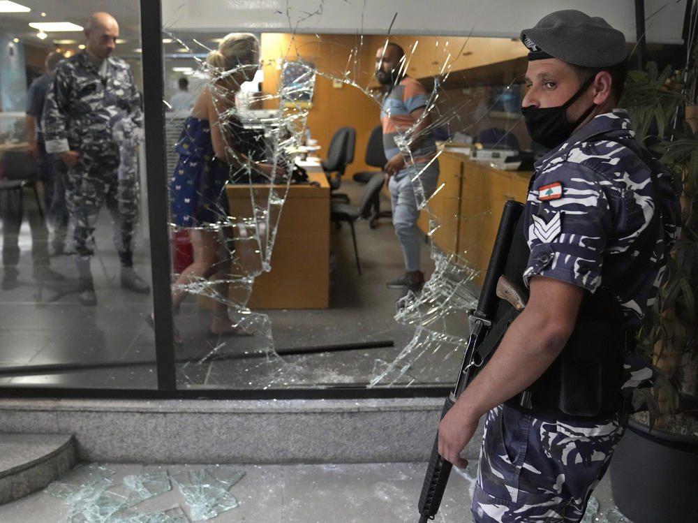A Lebanese policeman stands guard next to a window that was broken by depositors to exit the bank after attacking it trying to get their money, in Beirut.